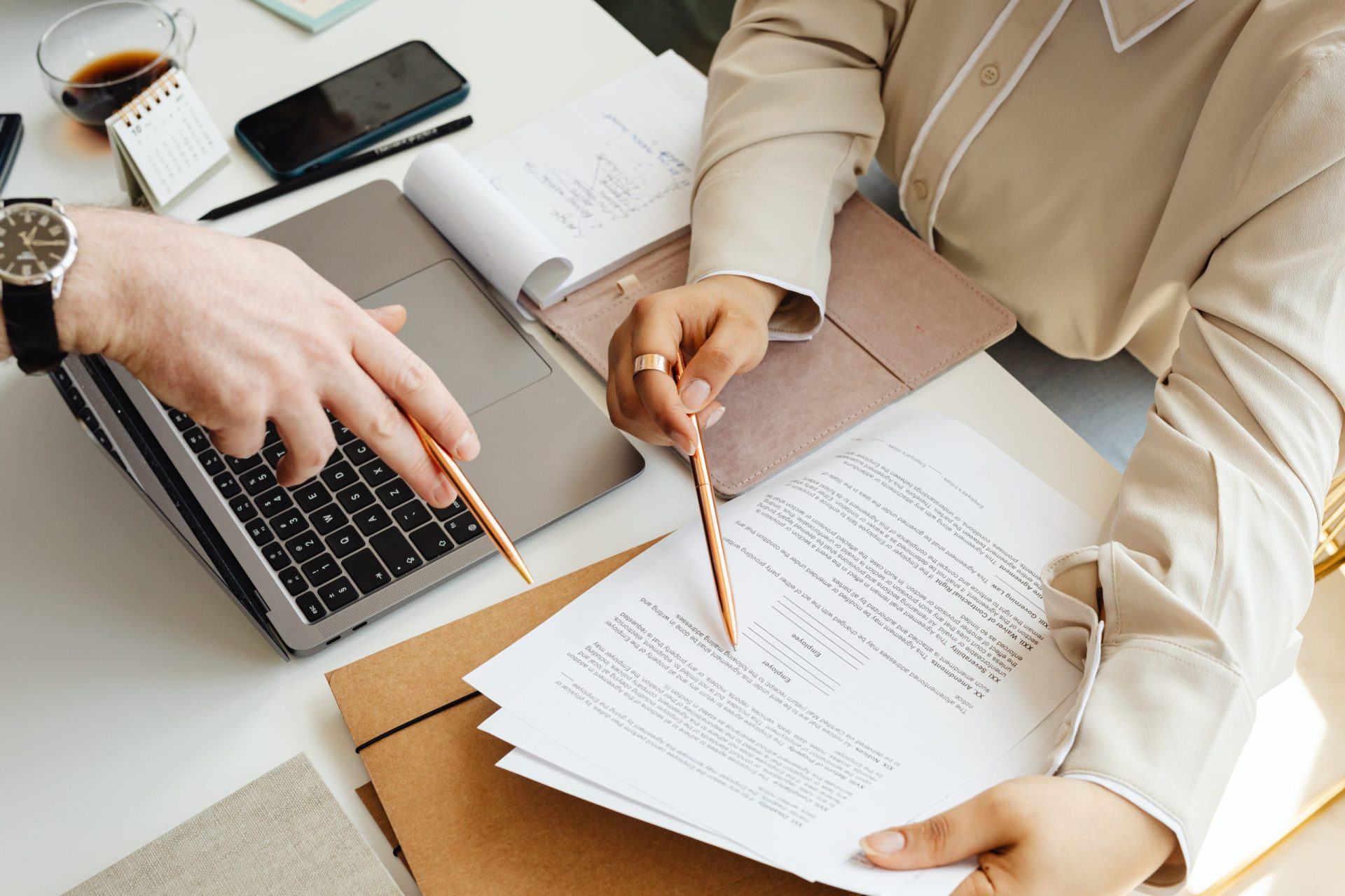 Two people reviewing and signing estate planning documents at a desk with a laptop.